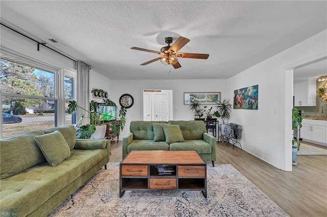 living area featuring a textured ceiling, wood finished floors, a ceiling fan, and baseboards