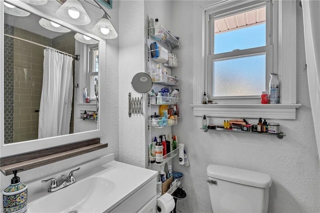 bathroom featuring toilet, vanity, tiled shower, and a textured wall