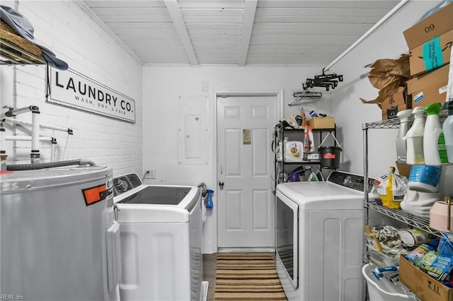 laundry area featuring electric water heater, laundry area, brick wall, wood finished floors, and independent washer and dryer