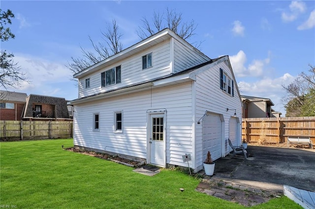 back of property featuring an attached garage, fence, aphalt driveway, and a lawn