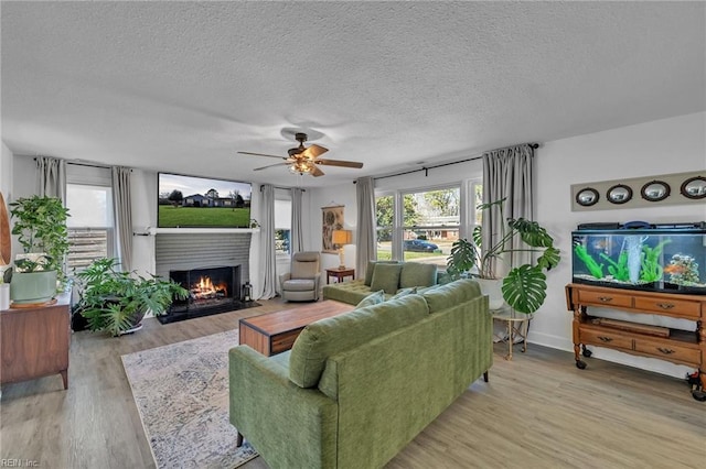 living room with light wood-style flooring, a ceiling fan, a textured ceiling, and a fireplace with flush hearth