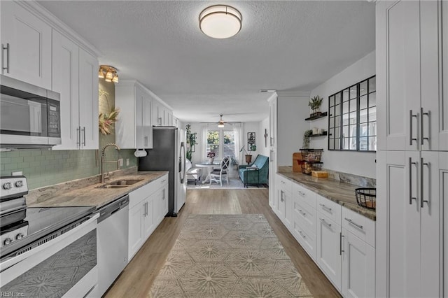 kitchen with appliances with stainless steel finishes, light wood-type flooring, white cabinetry, and a sink