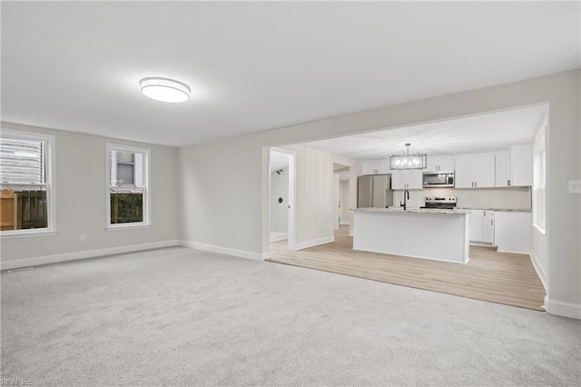 unfurnished living room featuring light carpet, a sink, a notable chandelier, and baseboards