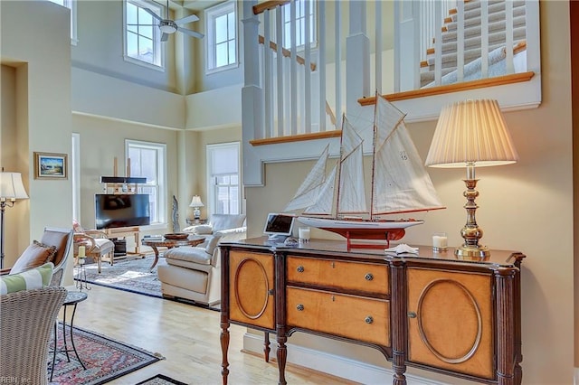 living room with a ceiling fan, light wood-style floors, and a high ceiling