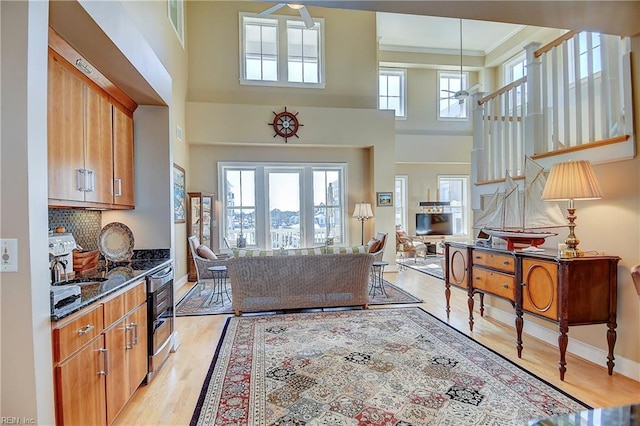 living room featuring crown molding, plenty of natural light, a towering ceiling, and light wood-style floors