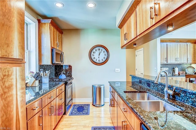 kitchen featuring stainless steel appliances, dark stone counters, brown cabinets, and a sink