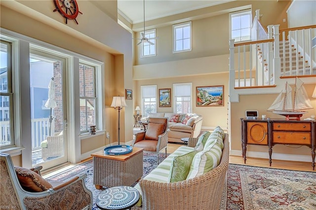 living area with a ceiling fan, a high ceiling, baseboards, and light wood finished floors