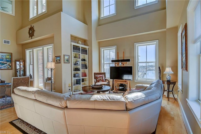 living room featuring light wood-style flooring, a high ceiling, plenty of natural light, and visible vents