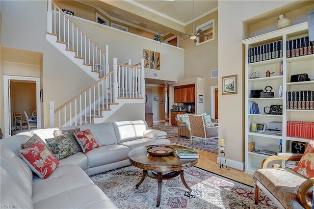 living room with crown molding, visible vents, a high ceiling, light wood-style floors, and stairs