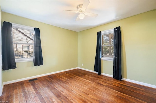 empty room featuring a ceiling fan, visible vents, baseboards, and wood finished floors