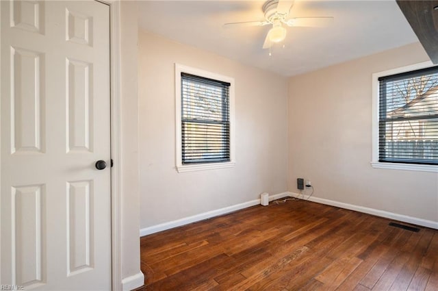 unfurnished room featuring plenty of natural light, baseboards, dark wood finished floors, and a ceiling fan