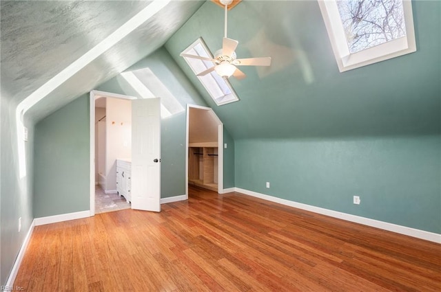 additional living space with a ceiling fan, vaulted ceiling with skylight, baseboards, and wood finished floors