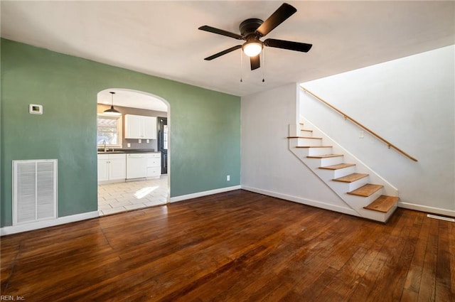 unfurnished living room featuring visible vents, arched walkways, baseboards, wood-type flooring, and stairway