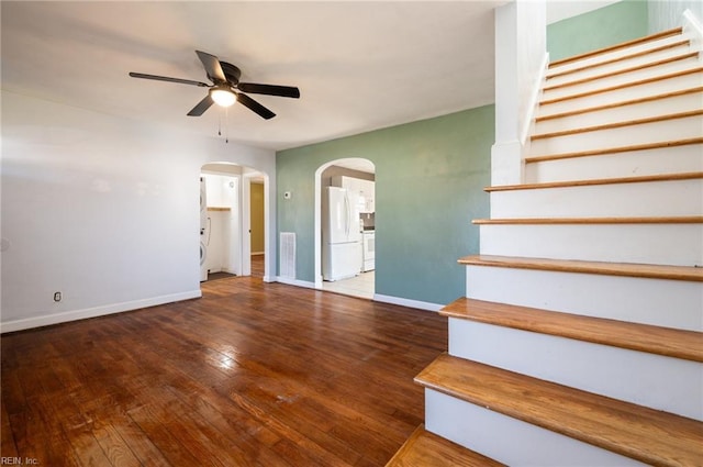 stairway featuring arched walkways, a ceiling fan, visible vents, baseboards, and hardwood / wood-style floors