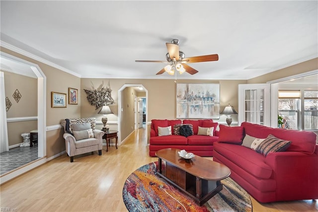 living area featuring arched walkways, ornamental molding, ceiling fan, light wood-type flooring, and baseboards