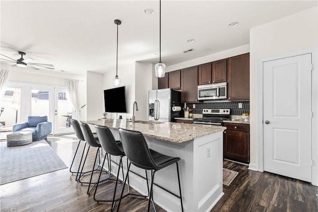 kitchen featuring stainless steel appliances, a sink, open floor plan, dark brown cabinets, and dark wood finished floors