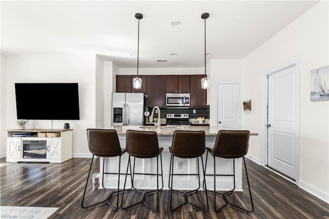 kitchen with decorative backsplash, appliances with stainless steel finishes, dark wood-type flooring, dark brown cabinets, and a kitchen bar