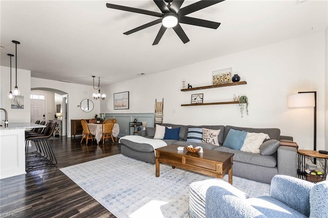 living room with dark wood-type flooring, arched walkways, and ceiling fan with notable chandelier