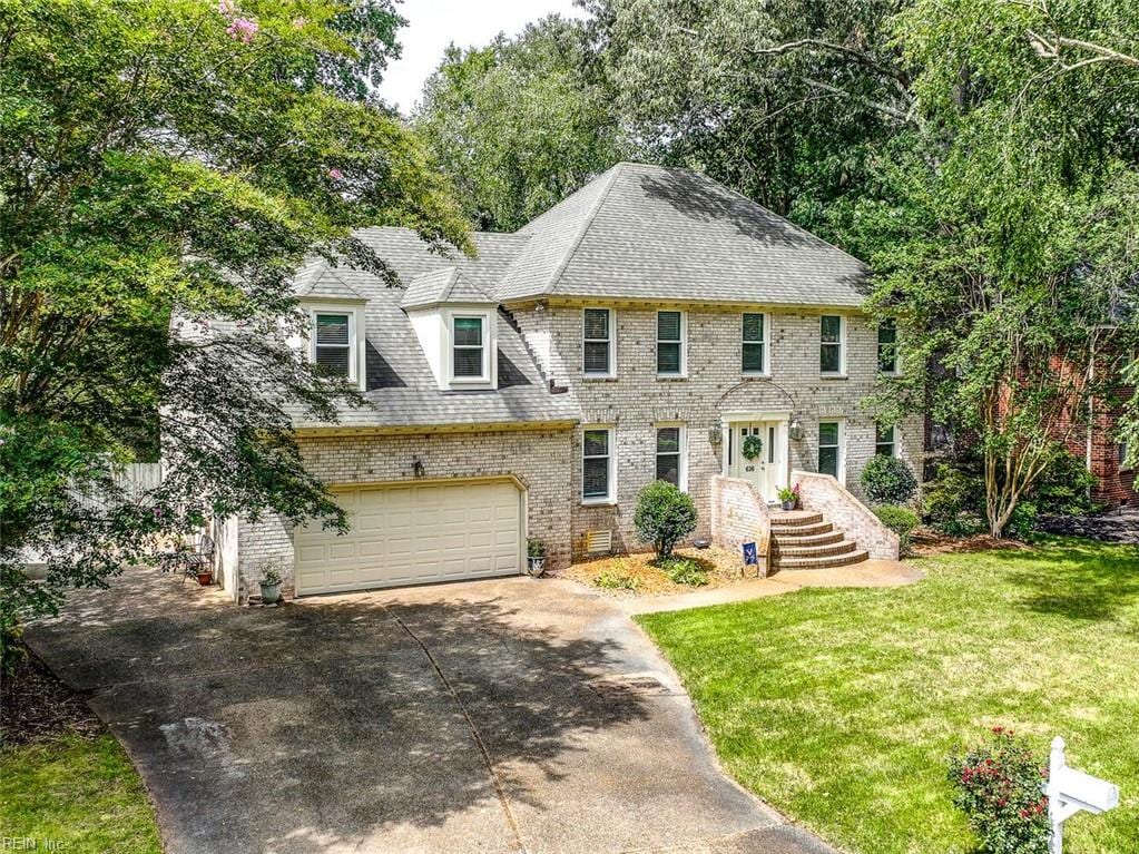 colonial house featuring driveway, a garage, roof with shingles, a front lawn, and brick siding