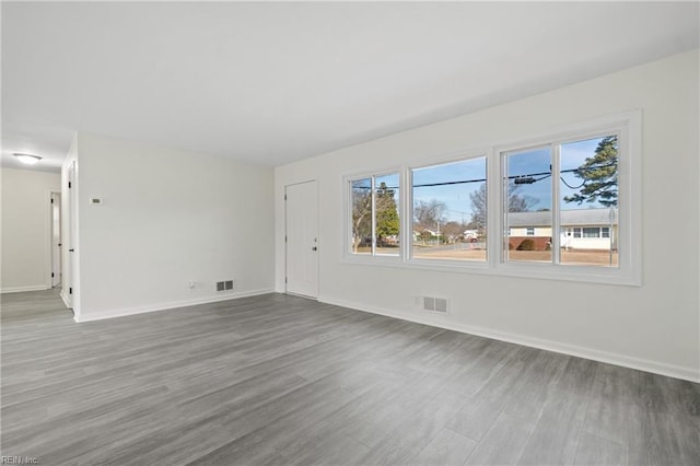 empty room with baseboards, visible vents, and wood finished floors