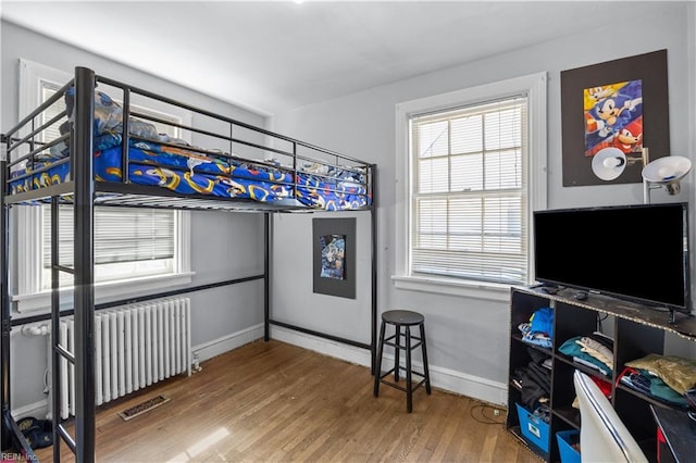 bedroom featuring baseboards, visible vents, radiator heating unit, and wood finished floors