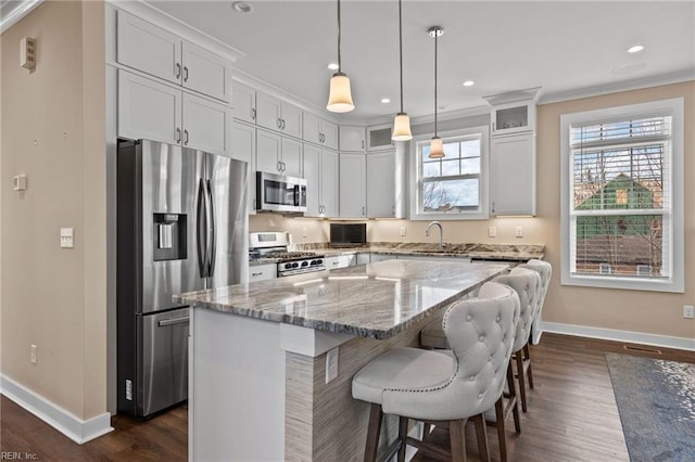 kitchen featuring a kitchen island, a sink, appliances with stainless steel finishes, light stone countertops, and glass insert cabinets