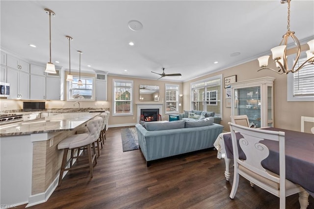 living area with a warm lit fireplace, dark wood finished floors, crown molding, and recessed lighting