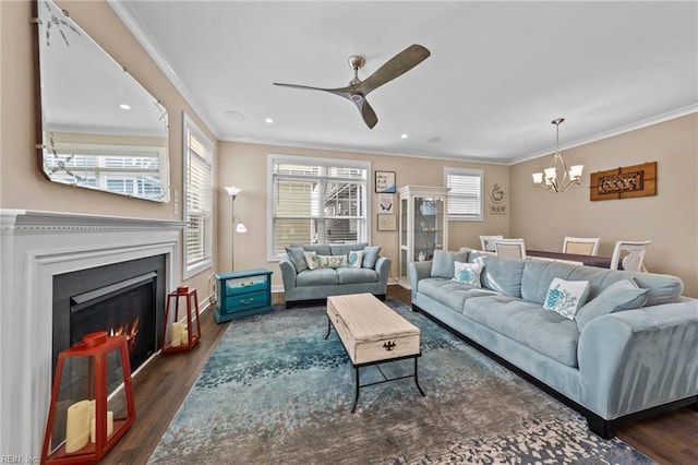 living area with baseboards, dark wood-style floors, a lit fireplace, crown molding, and ceiling fan with notable chandelier