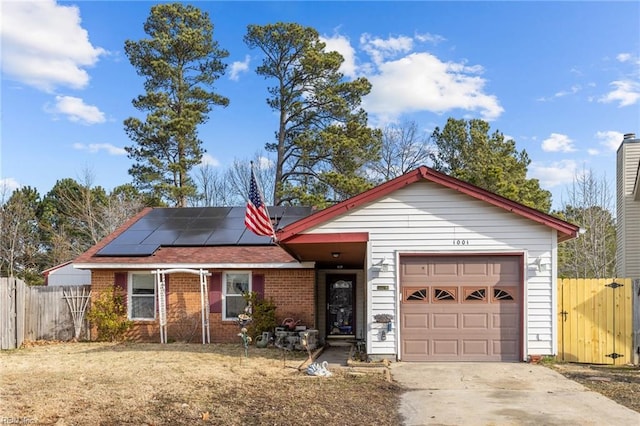 ranch-style house with brick siding, concrete driveway, roof mounted solar panels, fence, and a garage