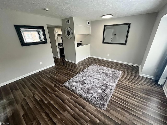 spare room featuring a textured ceiling, dark wood-style flooring, visible vents, and baseboards