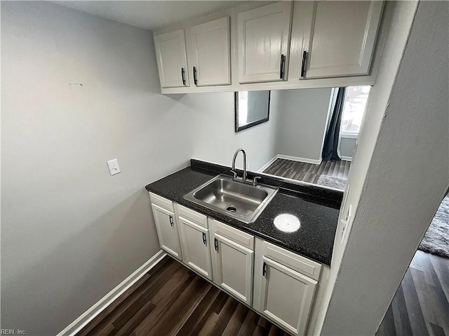 kitchen with baseboards, dark wood finished floors, dark countertops, white cabinetry, and a sink