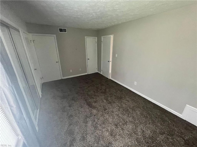 unfurnished bedroom featuring a textured ceiling, visible vents, baseboards, dark colored carpet, and two closets