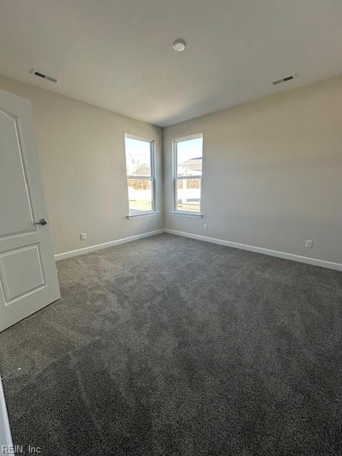 empty room featuring dark colored carpet, visible vents, and baseboards