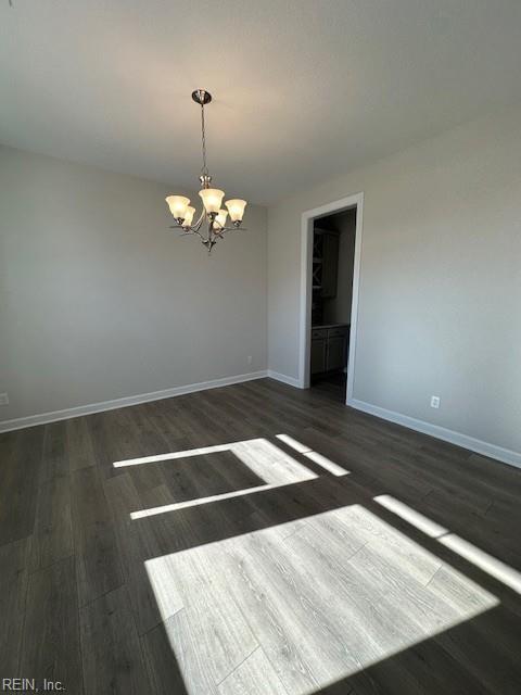 spare room with baseboards, dark wood-type flooring, and a notable chandelier