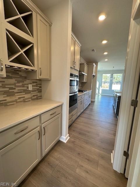 kitchen with double oven, gas stovetop, dark wood finished floors, and decorative backsplash