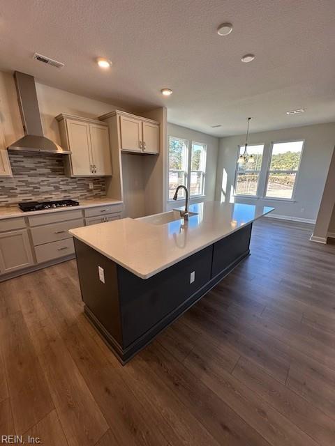 kitchen featuring black gas cooktop, dark wood-type flooring, a sink, visible vents, and wall chimney exhaust hood