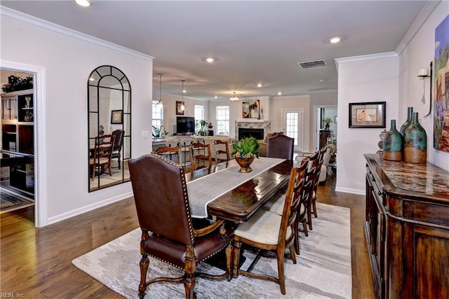 dining area with ornamental molding, visible vents, a fireplace, and wood finished floors