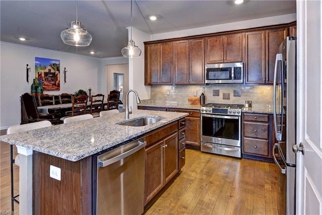 kitchen featuring a sink, a kitchen breakfast bar, appliances with stainless steel finishes, light wood finished floors, and tasteful backsplash