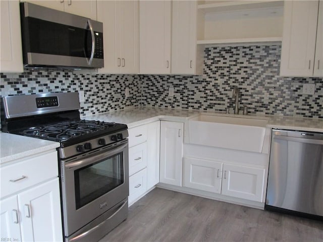 kitchen featuring a sink, light countertops, appliances with stainless steel finishes, light wood finished floors, and tasteful backsplash