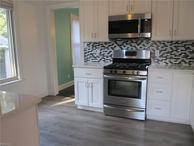 kitchen with stainless steel appliances, tasteful backsplash, white cabinetry, wood finished floors, and baseboards