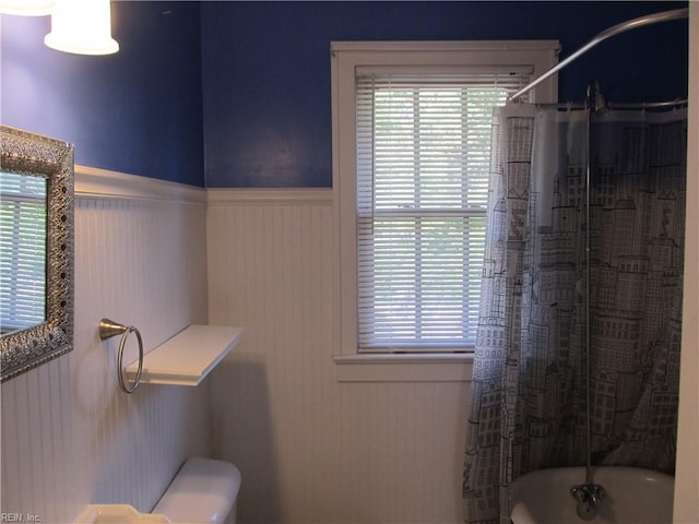 full bath with wainscoting, shower / bathtub combination with curtain, and toilet