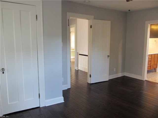 unfurnished bedroom with dark wood-style floors, ensuite bathroom, and baseboards