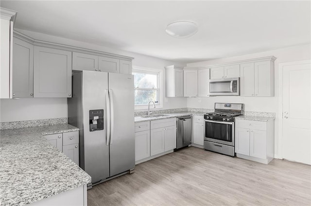 kitchen with stainless steel appliances, a sink, light wood finished floors, and light stone countertops