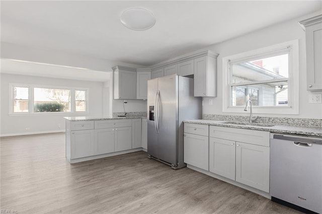 kitchen with light wood finished floors, baseboards, light stone counters, stainless steel appliances, and a sink