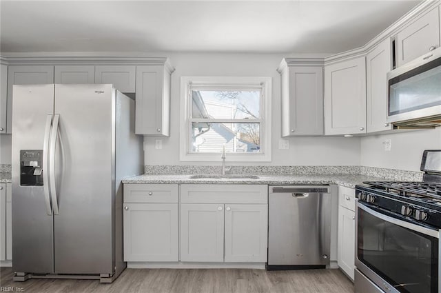 kitchen with light wood finished floors, white cabinets, light stone countertops, stainless steel appliances, and a sink