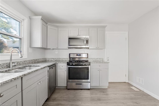 kitchen featuring stainless steel appliances, a sink, visible vents, light wood-type flooring, and light stone countertops