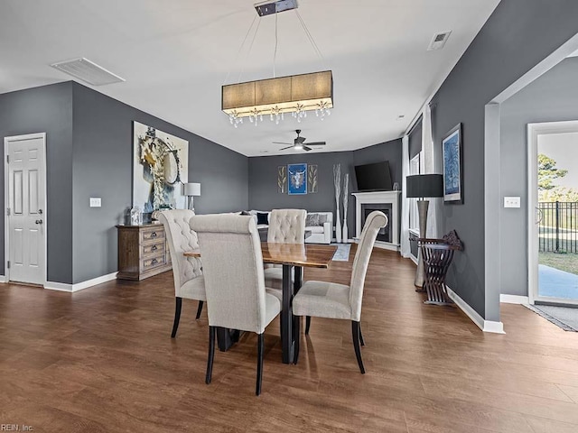 dining space featuring a ceiling fan, a fireplace, visible vents, and wood finished floors