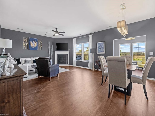 dining room featuring dark wood-style floors, ceiling fan with notable chandelier, a wealth of natural light, and a glass covered fireplace