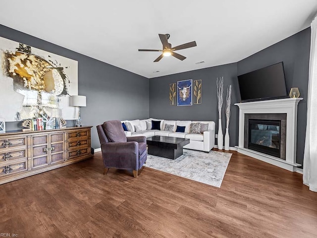 living area with a ceiling fan, a glass covered fireplace, baseboards, and wood finished floors