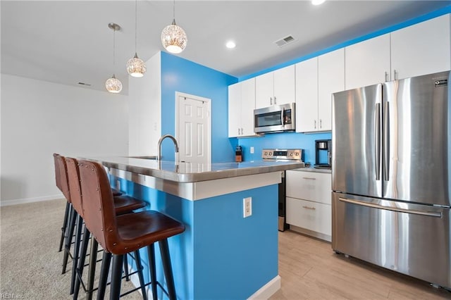 kitchen featuring recessed lighting, white cabinets, appliances with stainless steel finishes, a center island with sink, and pendant lighting